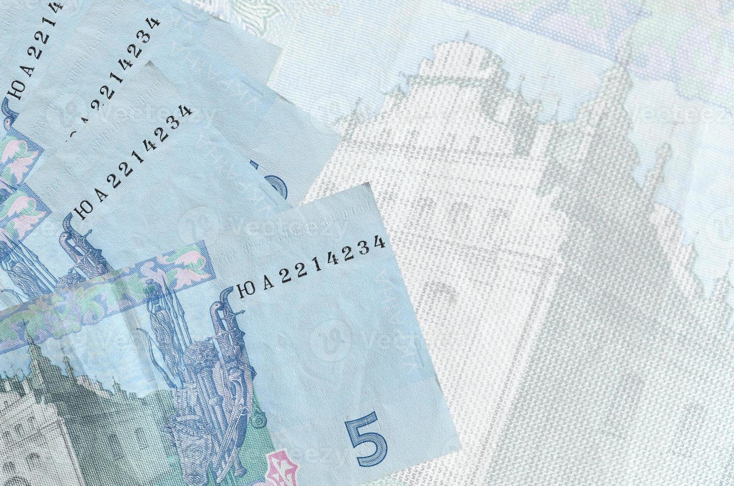 5 Ukrainian hryvnias bills lies in stack on background of big semi-transparent banknote. Abstract business background photo