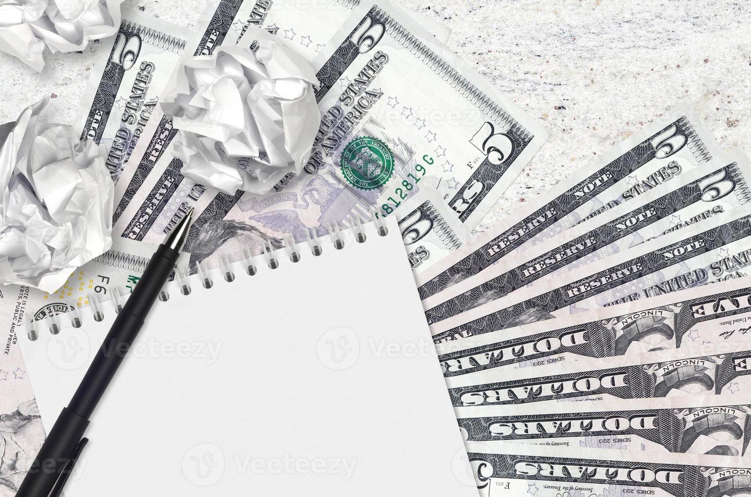 5 US dollars bills and balls of crumpled paper with blank notepad. Bad ideas or less of inspiration concept. Searching ideas for investment photo