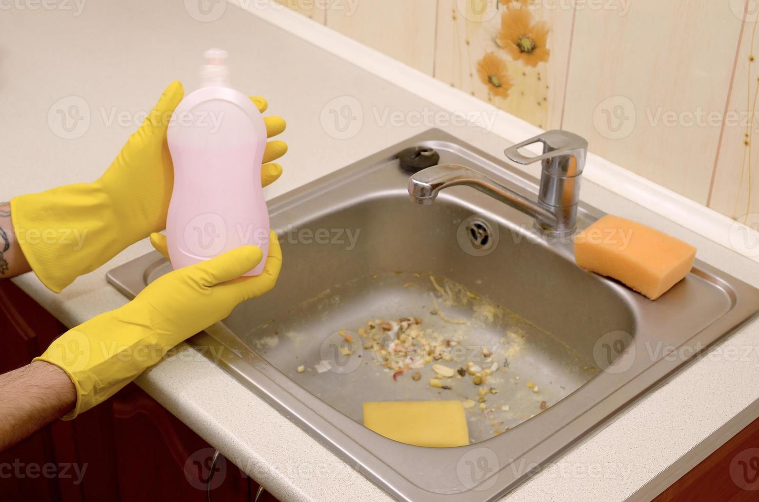 Cleaner shows liquid cleanser detergent bottle at dirty kitchen sink with food particles before the cleaning photo