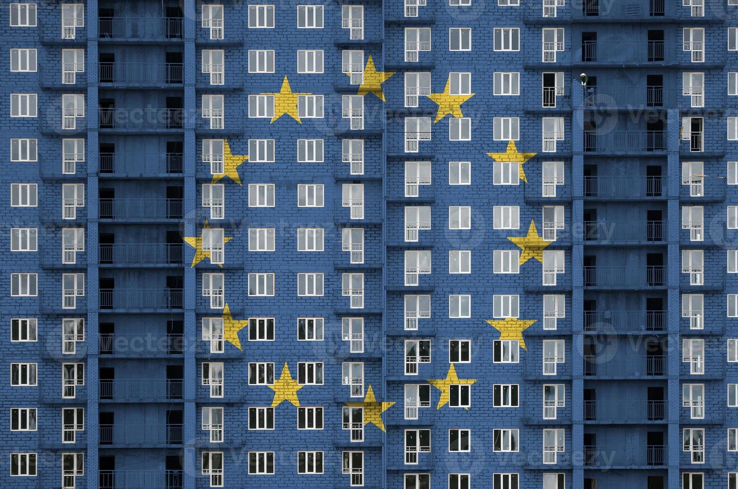 European union flag depicted in paint colors on multi-storey residental building under construction. Textured banner on brick wall background photo