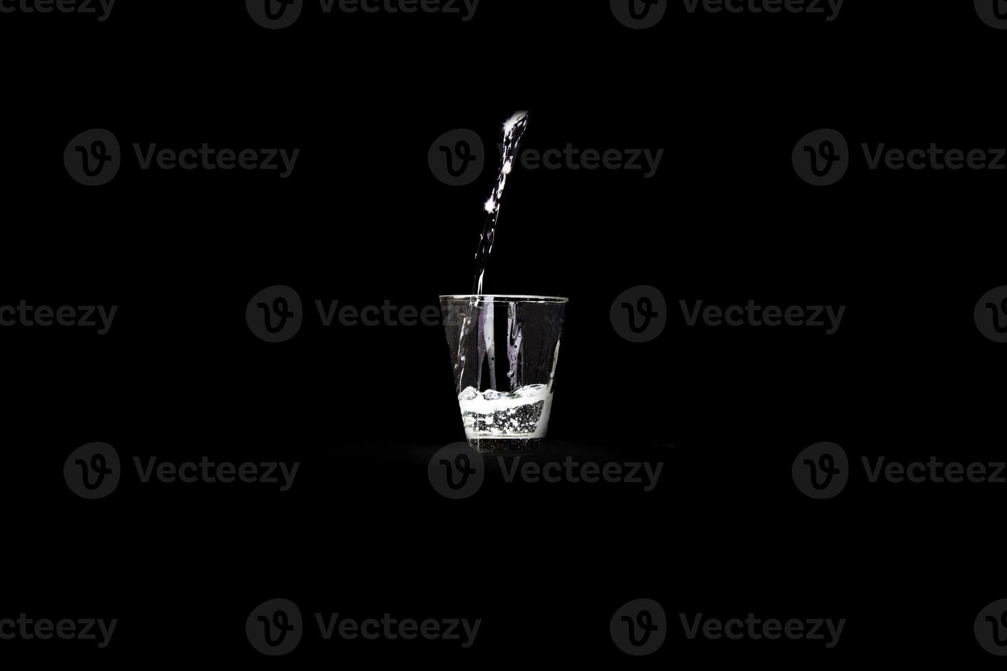 A glass of water with a stream of falling water against an infinite black background photo