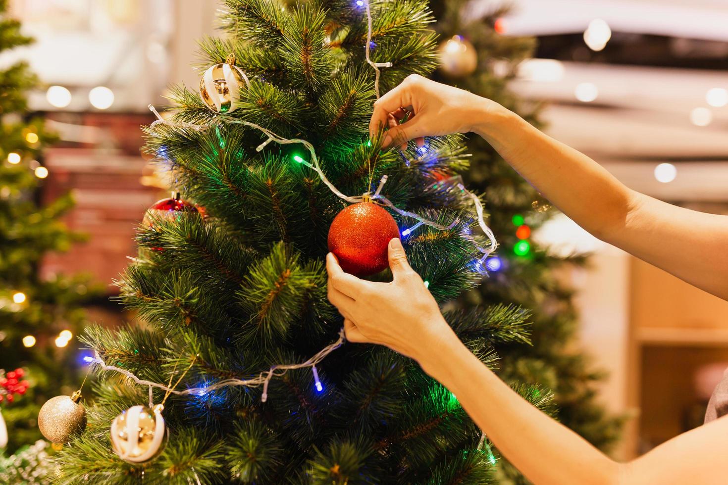 la mano de la mujer cuelga una bola de navidad en el árbol de navidad festivo. foto