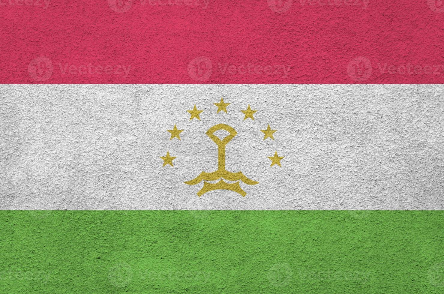 Tajikistan flag depicted in bright paint colors on old relief plastering wall. Textured banner on rough background photo