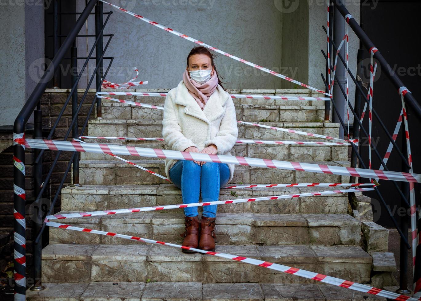 Photo of a girl in a mask. Sitting on the street with danger warning tapes.