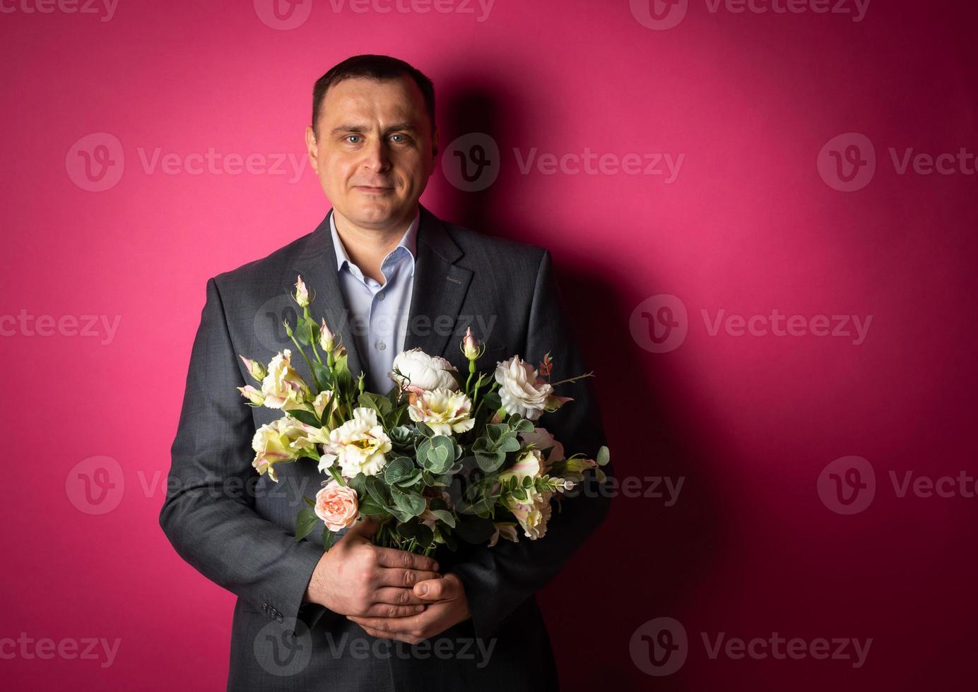 un apuesto hombre de negocios con traje mira a la cámara con un ramo de flores. foto