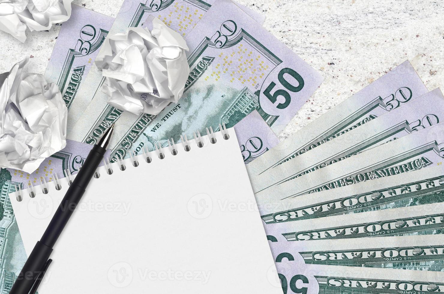 50 US dollars bills and balls of crumpled paper with blank notepad. Bad ideas or less of inspiration concept. Searching ideas for investment photo