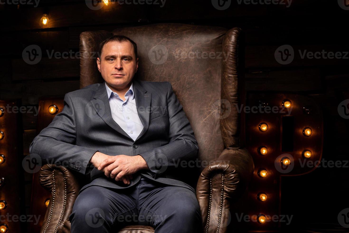 handsome businessman in a suit looks at the camera on a leather chair. photo