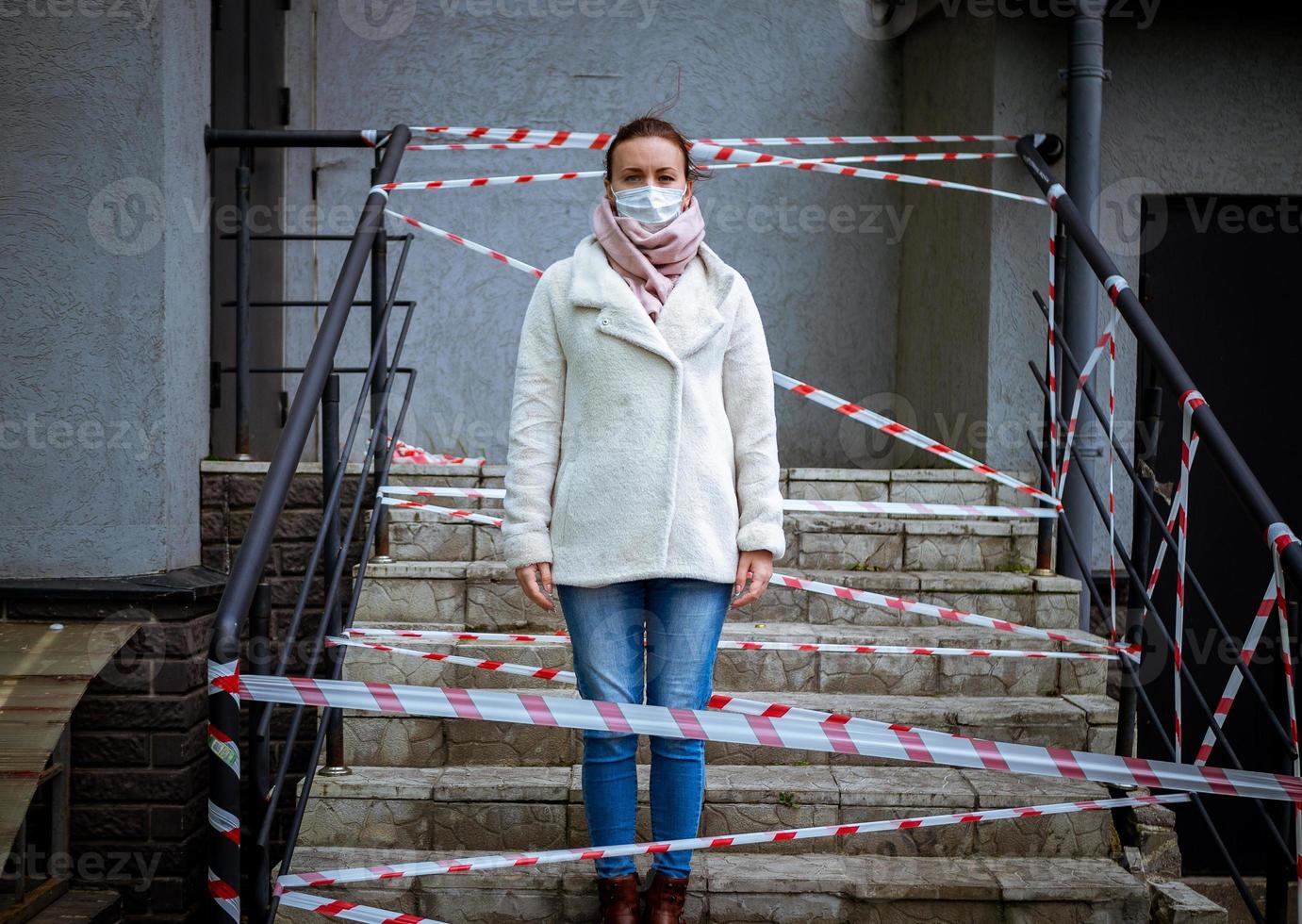 Photo of a girl in a mask. Standing on the street with danger warning tapes.