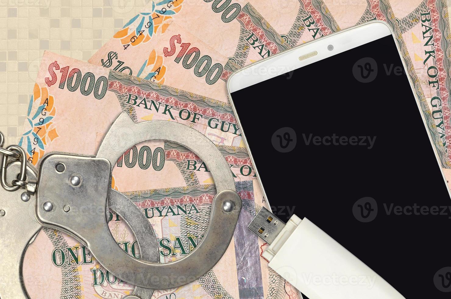 1000 Guyanese dollars bills and smartphone with police handcuffs. Concept of hackers phishing attacks, illegal scam or malware soft distribution photo