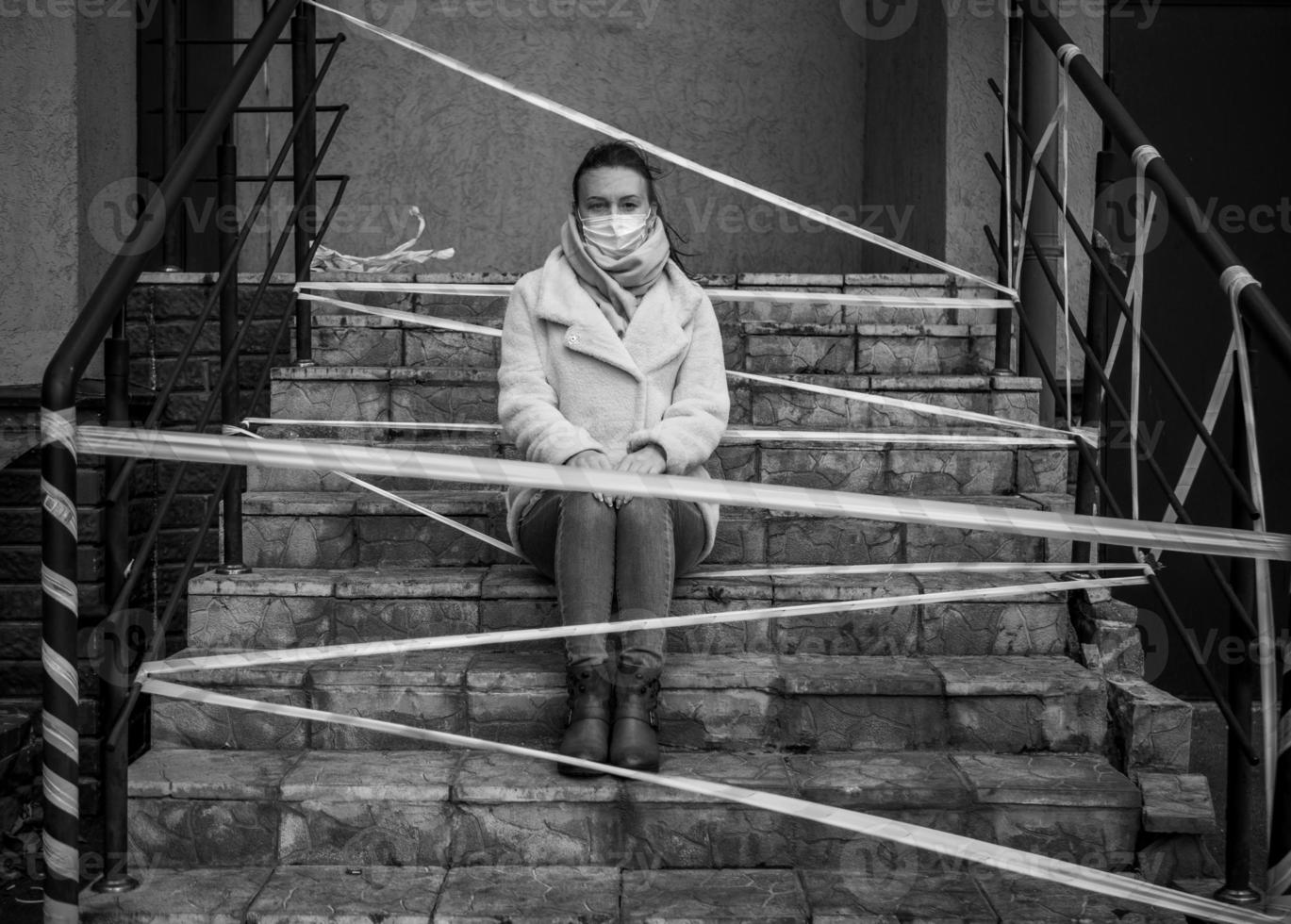 Photo of a girl in a mask. Sitting on the street with danger warning tapes.