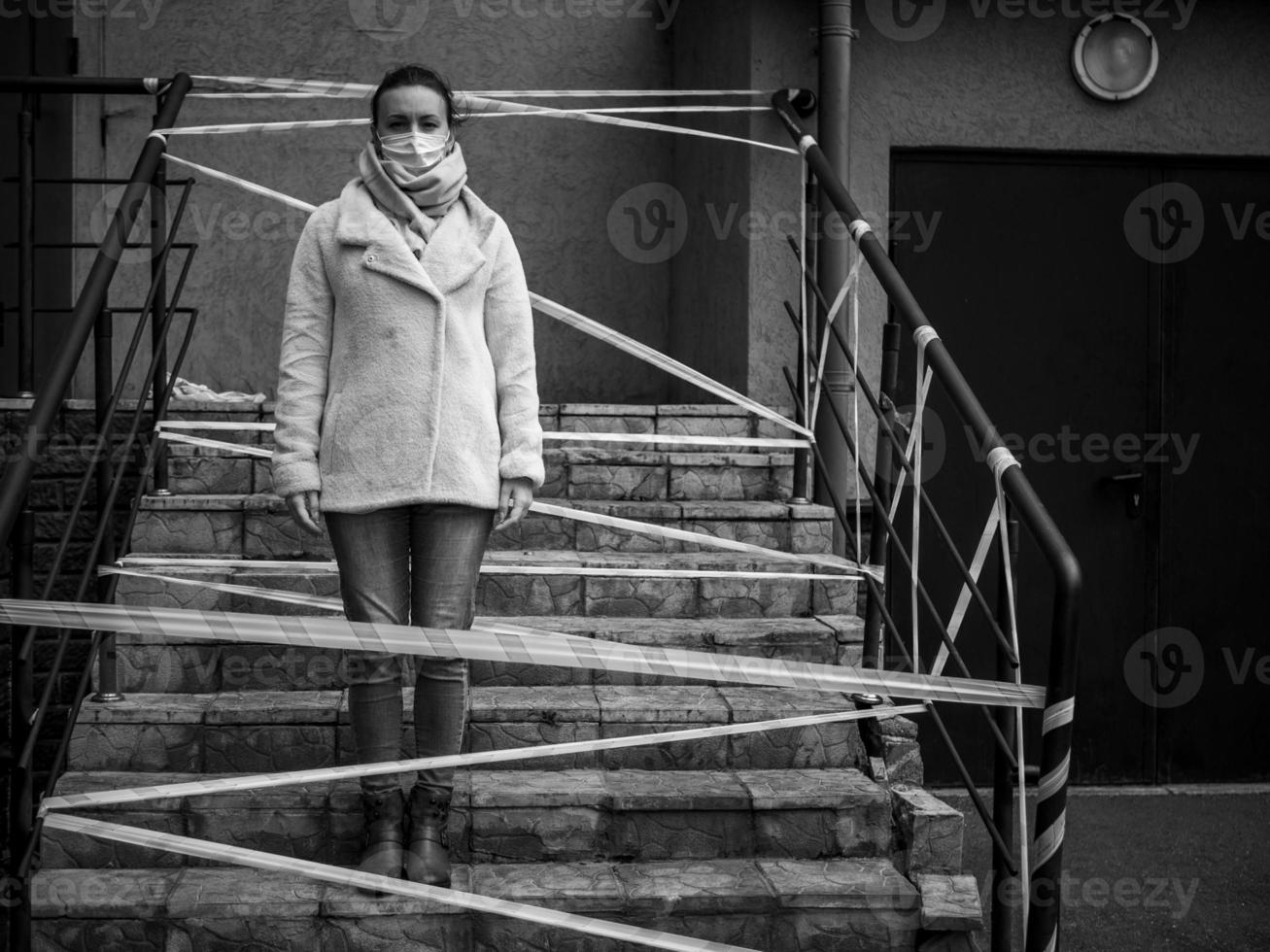 Photo of a girl in a mask. Standing on the street with danger warning tapes.