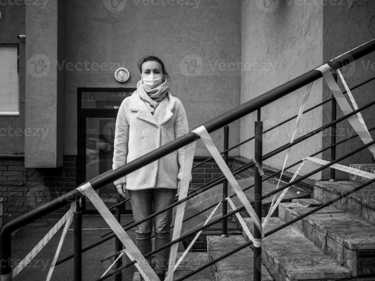 Photo of a girl in a mask. Standing on the street with danger warning tapes.