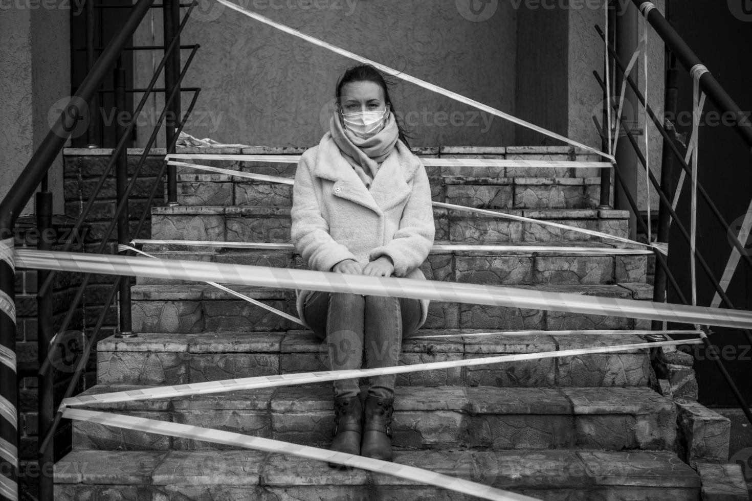 Photo of a girl in a mask. Sitting on the street with danger warning tapes.