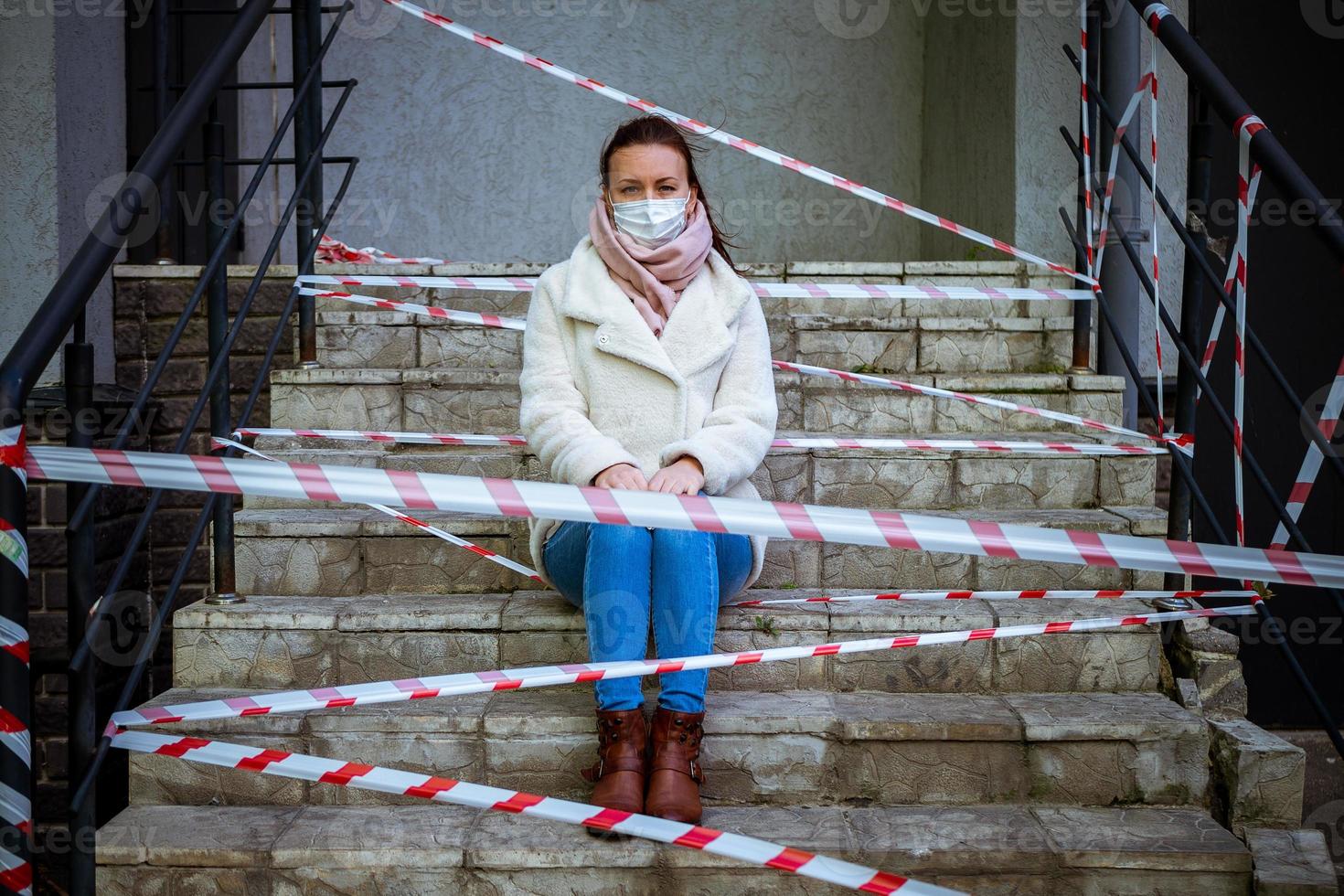 Photo of a girl in a mask. Sitting on the street with danger warning tapes.