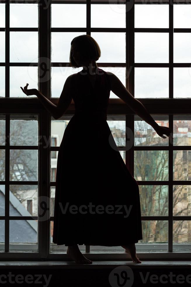 Silhouette of woman with head turned in front of window photo
