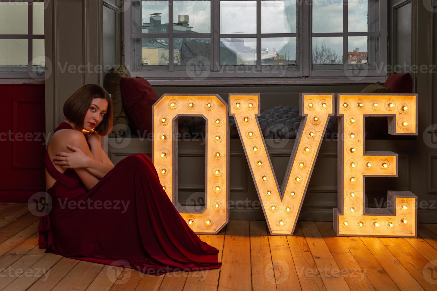 Woman with crossed arms in red dress making letter L in front of LOVE letters photo