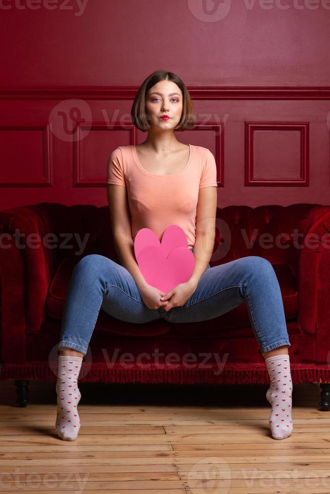 mujeres en jeans con las piernas abiertas sentadas en el sofá y sosteniendo formas de corazón foto