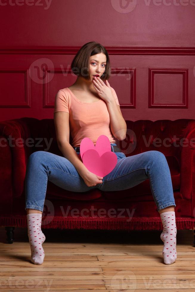Women in jeans with open legs sitting on couch and holding heart shapes
