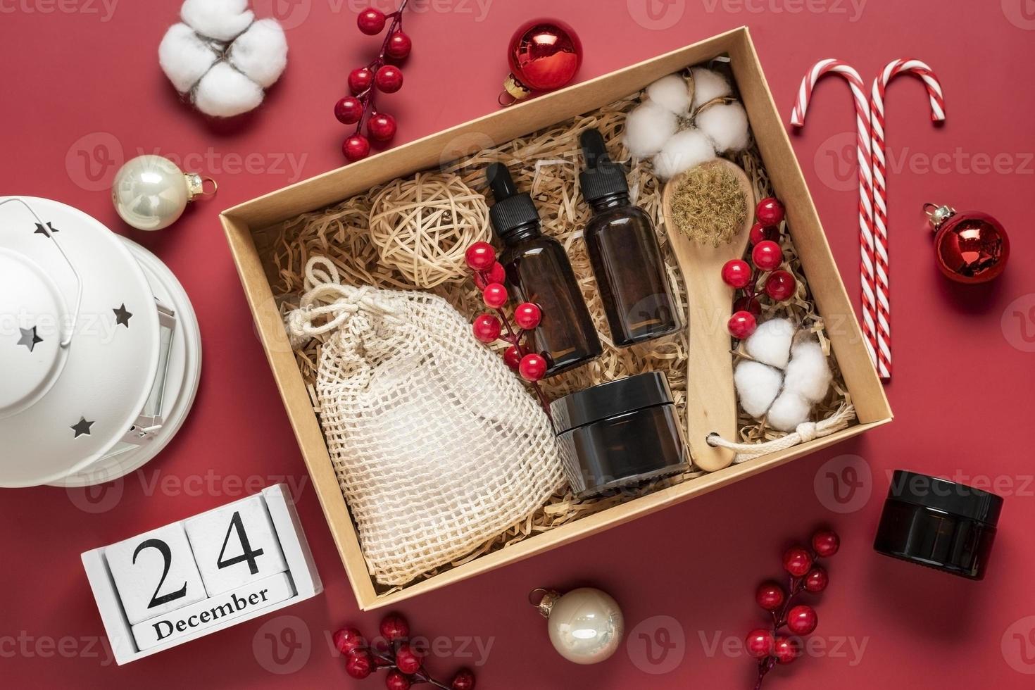Set for care box Eco-friendly cosmetics Oil and cream bottles, brush for washing, cotton pads on red background Gift for girlfriend, mother to celebrate Christmas concept Top view Flat lay photo