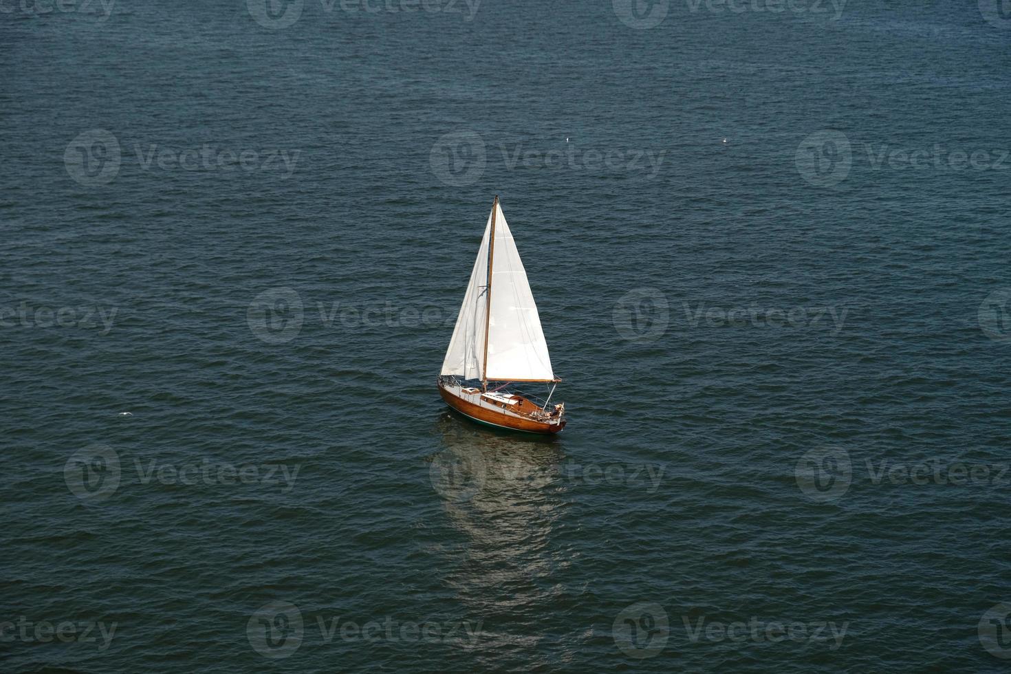 Aerial view of wooden old yacht with sail against backdrop of blue water with waves and ripples. Lonely white sail is sailing. Perfect content for posters or advertising banners, creative projects. photo