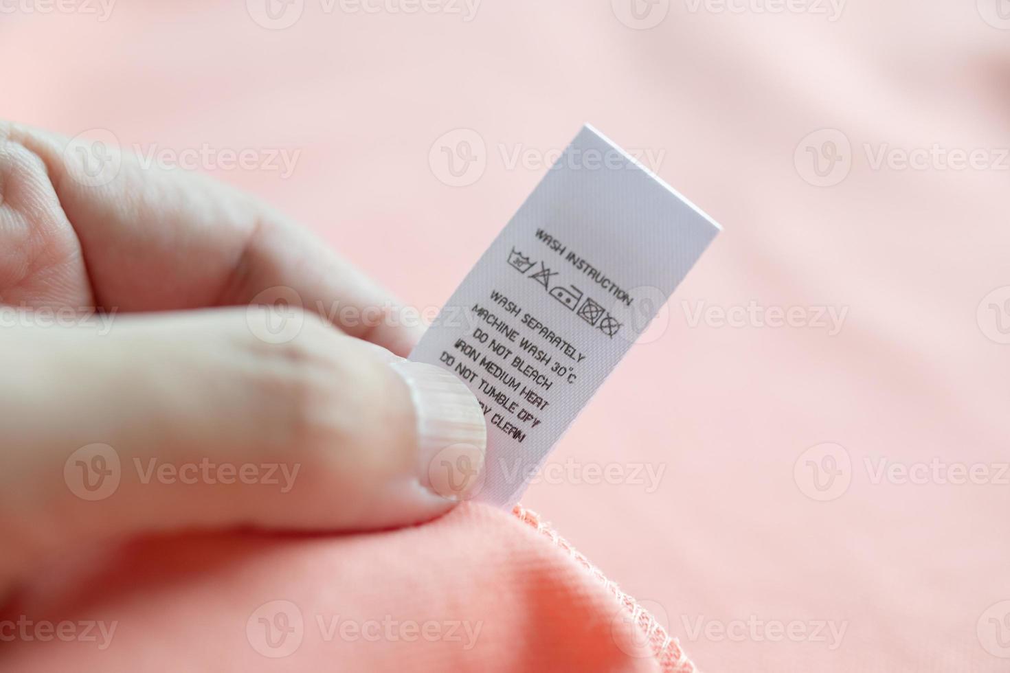 Hand hold and reading at white laundry care washing instructions clothes label on pink shirt photo