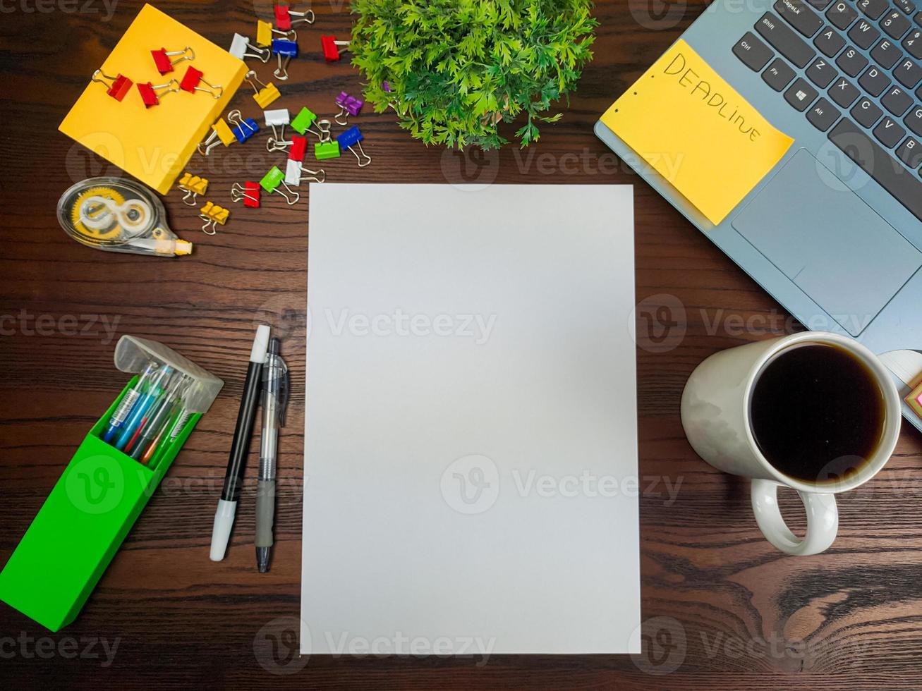 endecha plana, papel simulado. espacio de trabajo en el fondo del escritorio de la oficina desde la vista superior. con papel blanco en blanco, computadoras portátiles, útiles de oficina, lápices, hojas verdes y tazas de café en una mesa de madera. foto