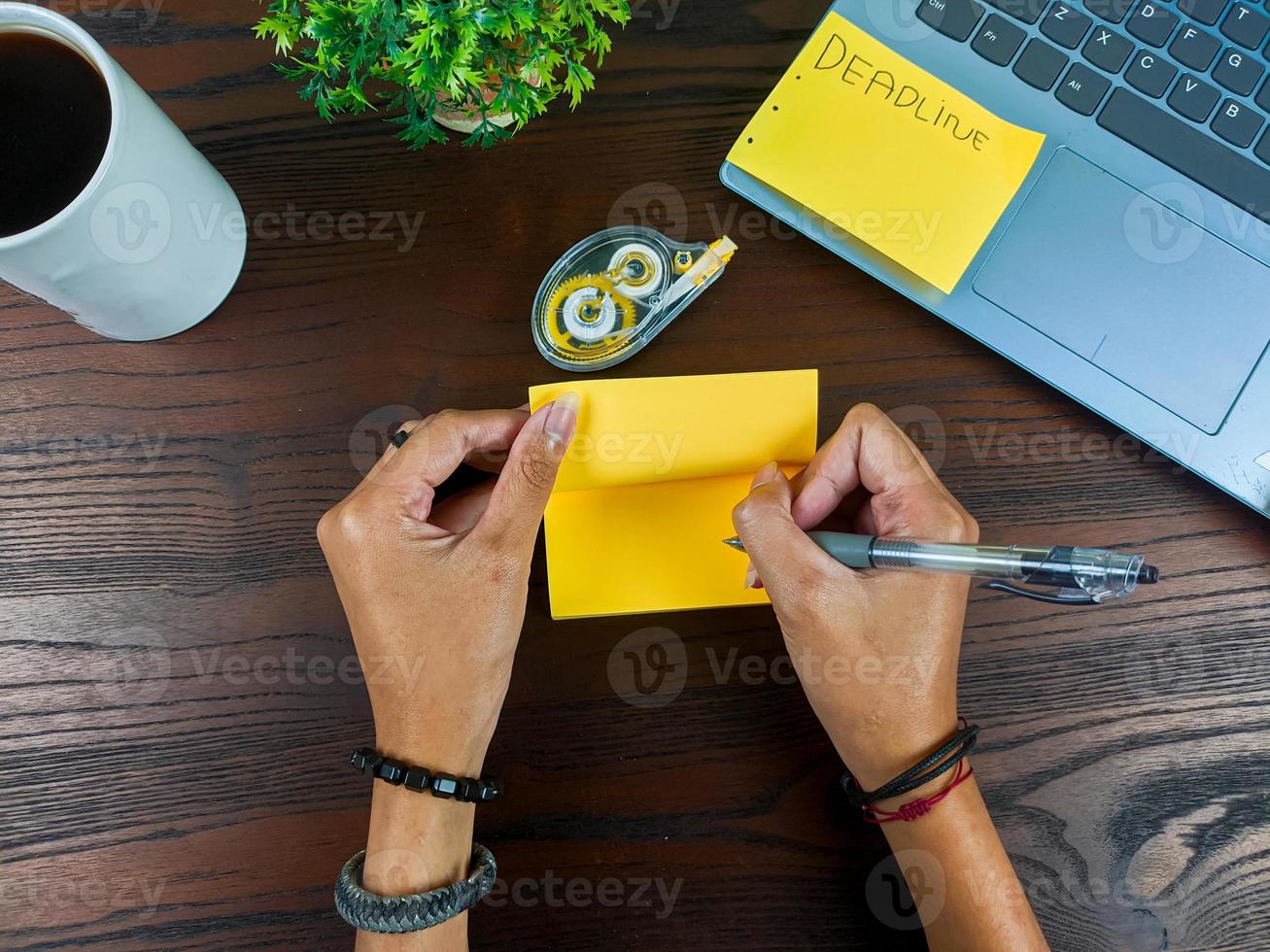 las mujeres escriben en notas amarillas, se burlan de las notas amarillas. las manos de las mujeres escriben notas en papel amarillo en el fondo del espacio de trabajo de la oficina desde la vista superior. foto