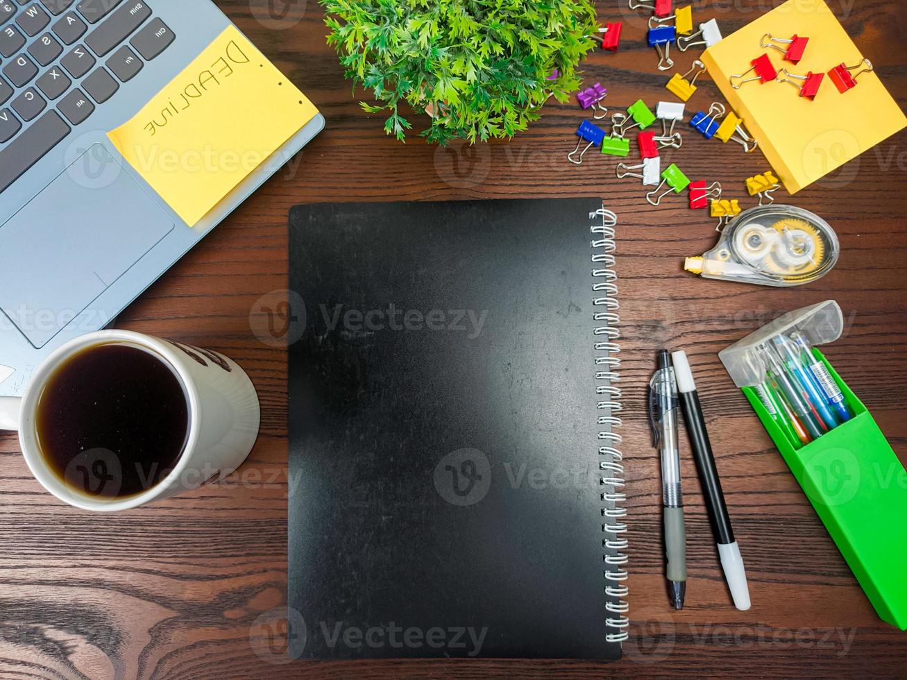 endecha plana, maqueta de libro negro. espacio de trabajo en el fondo del escritorio de la oficina desde la vista superior. con libros negros, computadoras portátiles, material de oficina, lápices, hojas verdes y tazas de café en la mesa de madera. foto