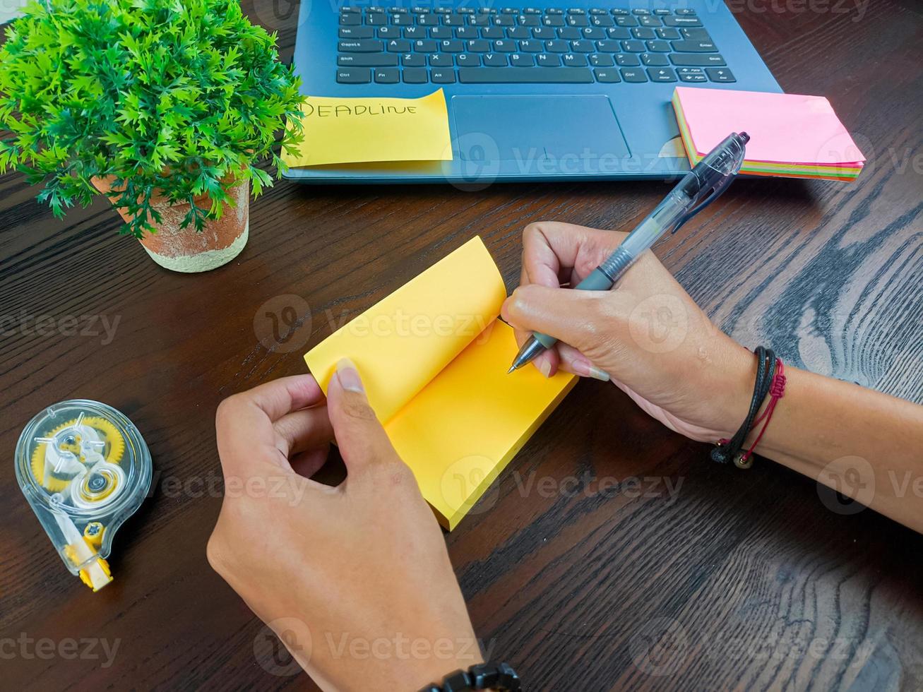 las mujeres escriben en notas amarillas, se burlan de las notas amarillas. las manos de las mujeres escriben notas en papel amarillo en el fondo del espacio de trabajo de la oficina desde la vista superior. foto