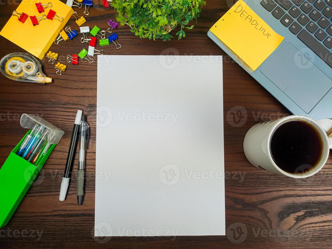 endecha plana, papel simulado. espacio de trabajo en el fondo del escritorio de la oficina desde la vista superior. con papel blanco en blanco, computadoras portátiles, útiles de oficina, lápices, hojas verdes y tazas de café en una mesa de madera. foto