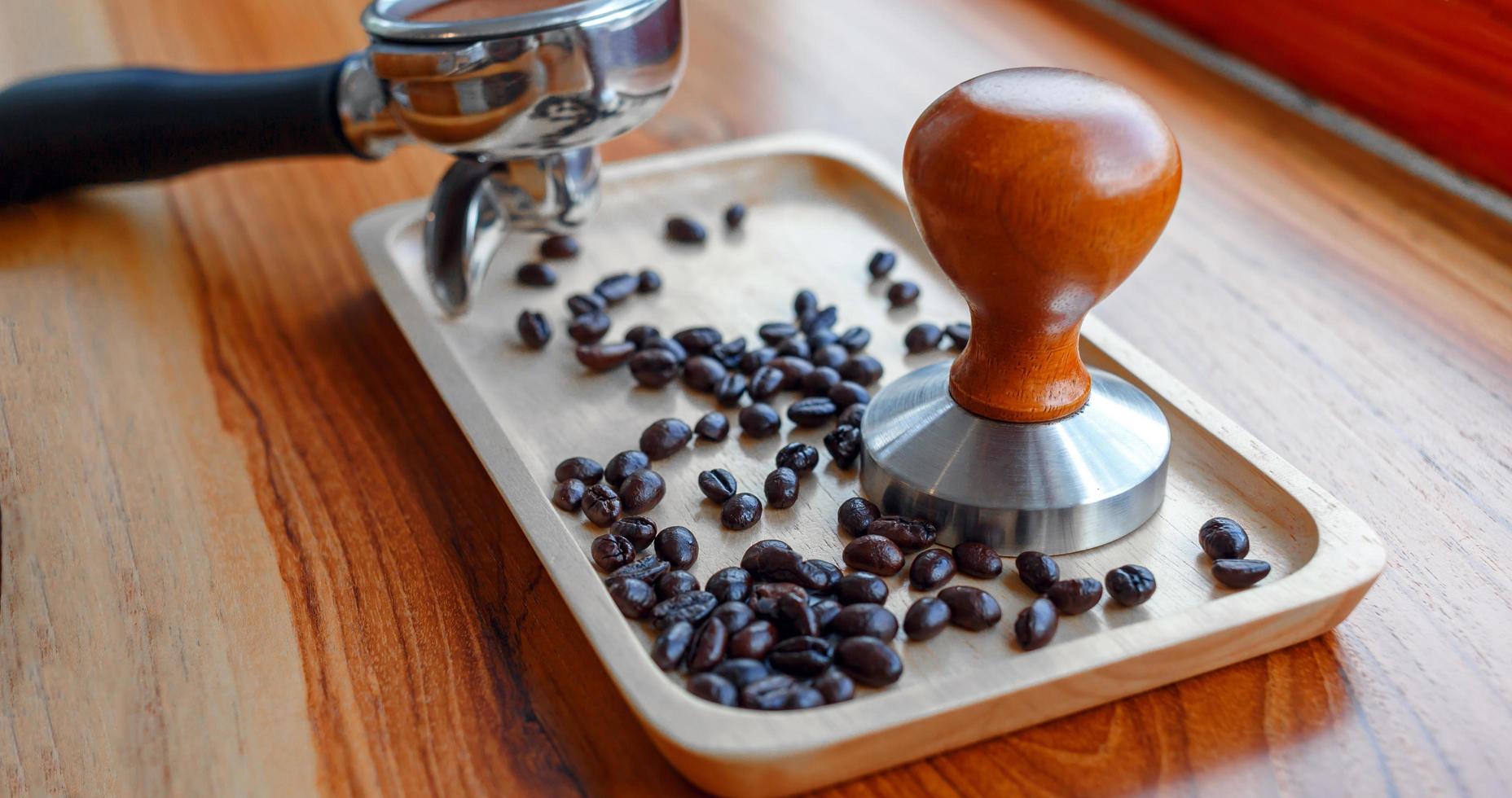 equipo de manipulación de herramientas de café barista y café templado en granos de café tostados de portafiltro sobre mesa de madera foto