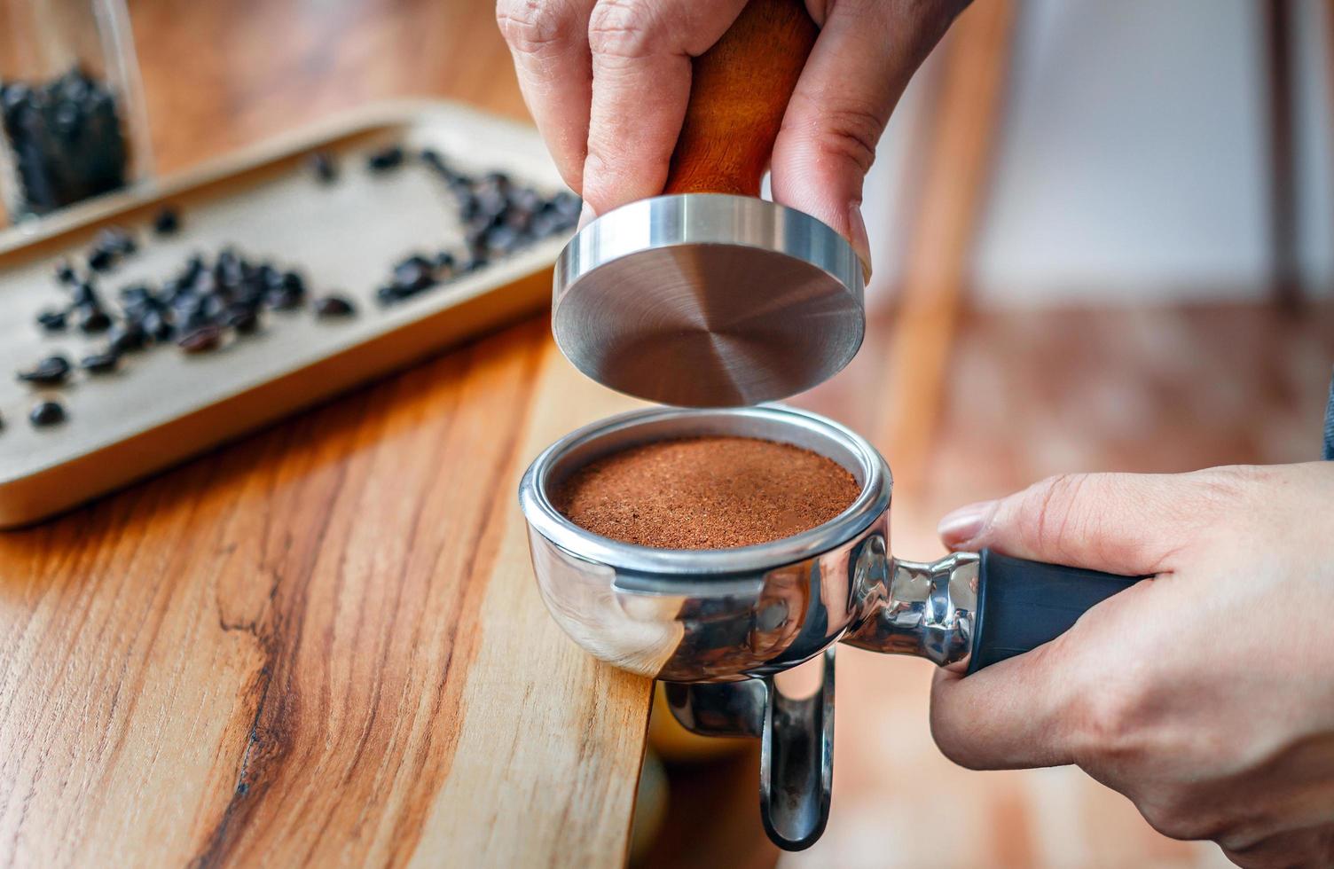 Close-up of hand Barista cafe making coffee with manual presses ground coffee using tamper on the wooden counter bar at the coffee shop photo