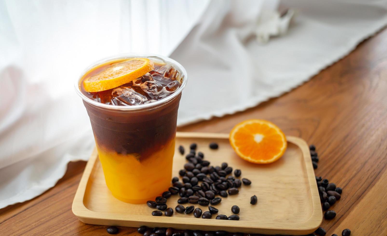 menú de bebidas de café helado naranja americano con fruta fresca de naranja mezclada en un vaso de plástico en el mostrador de madera de la cafetería foto