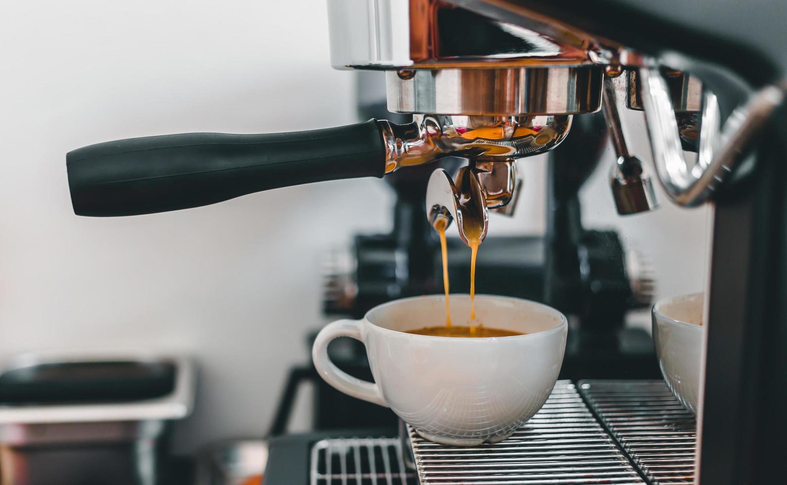 extracción de café de la máquina de café con un portafiltro que vierte café en una taza, espresso de la máquina de café en la cafetería foto