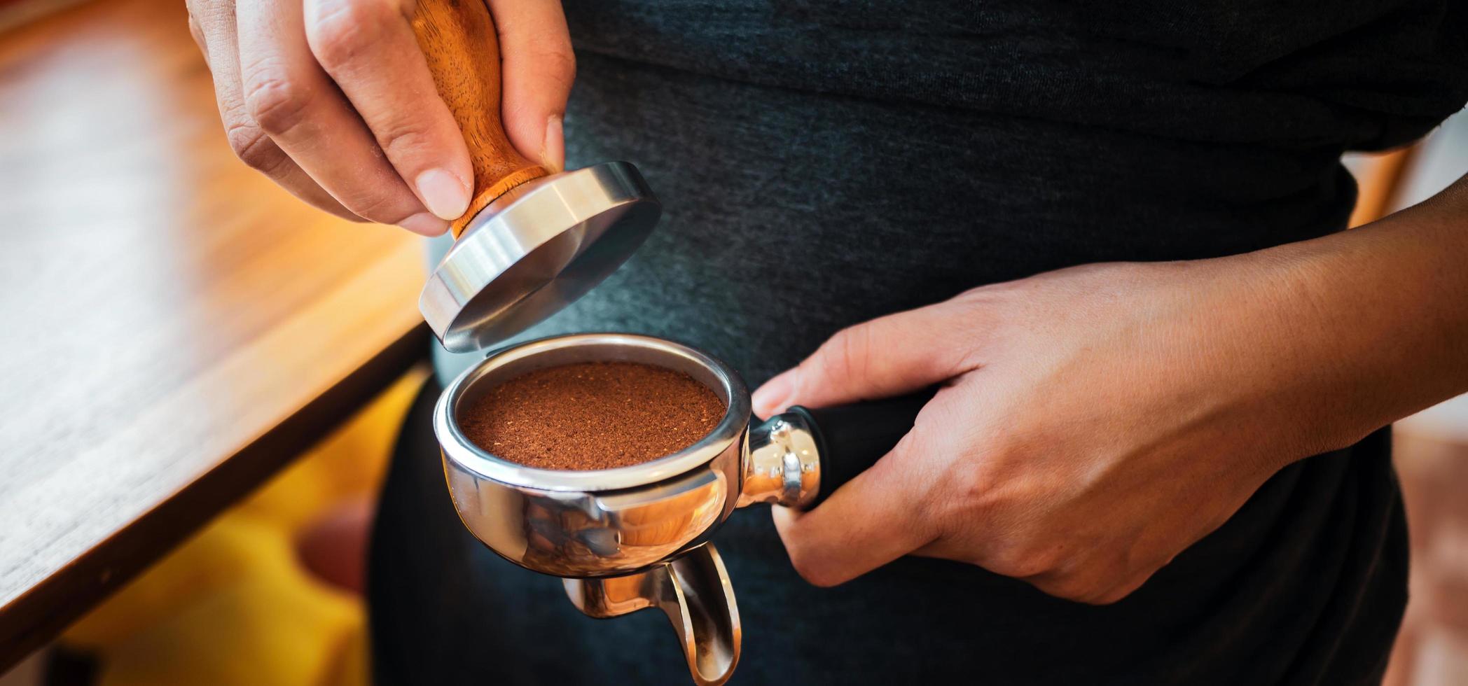 Close-up of hand Barista cafe making coffee with manual presses ground coffee using tamper at the coffee shop photo