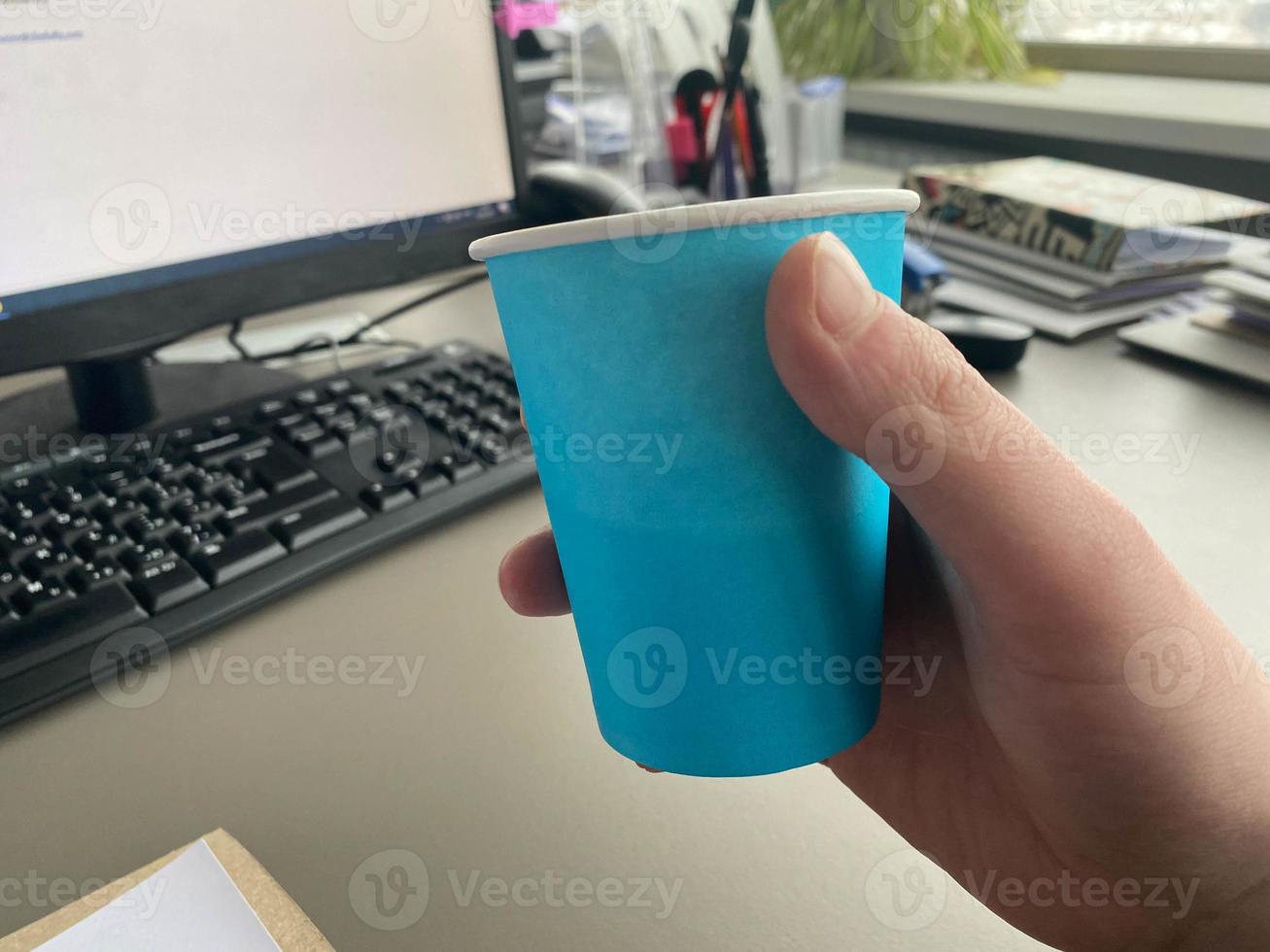 Cardboard blue coffee cup from a coffee shop on a desktop with a computer with a keyboard and mouse and office supplies of an office worker during lunch. Business coffee break photo