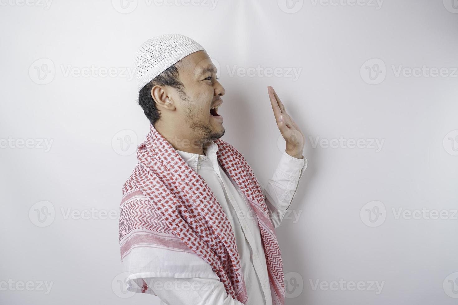 Excited Asian Muslim man pointing at the copy space beside him, isolated by white background photo