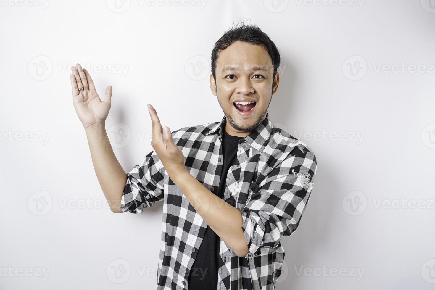 Smiling Asian man wearing tartan shirt is pointing at the copy space on top of him, isolated by white background photo