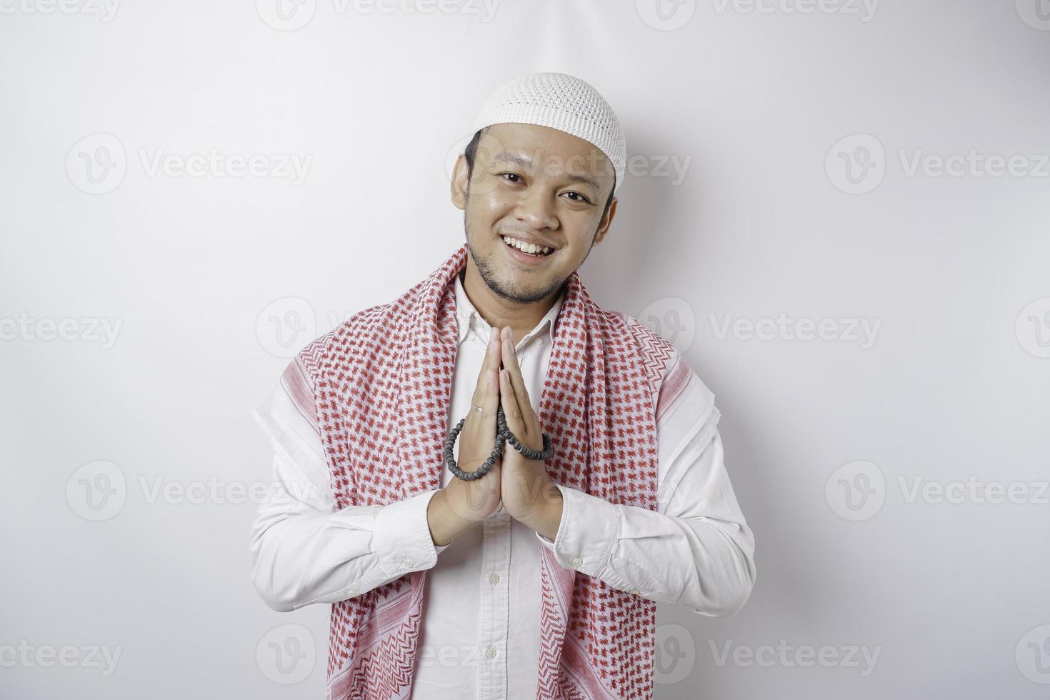 Smiling young Asian Muslim man, gesturing traditional greeting isolated over white background photo