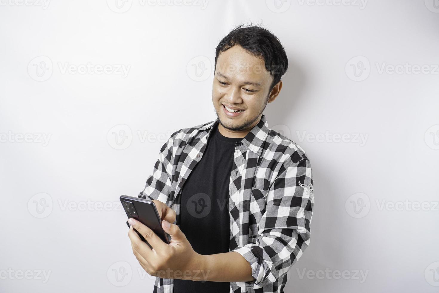 A portrait of a happy Asian man is smiling while holding on his phone, isolated by white background photo