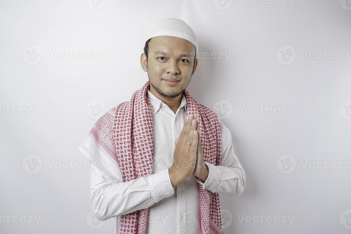 Smiling young Asian Muslim man, gesturing traditional greeting isolated over white background photo