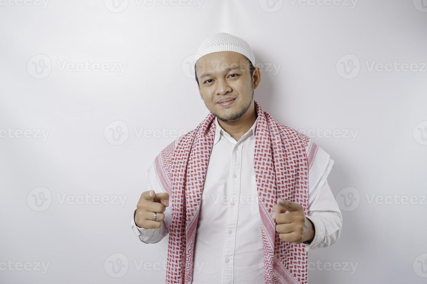 joven musulmán asiático parado sobre un fondo blanco aislado señalando con el dedo a la cámara con cara feliz. buena energia y vibras. foto