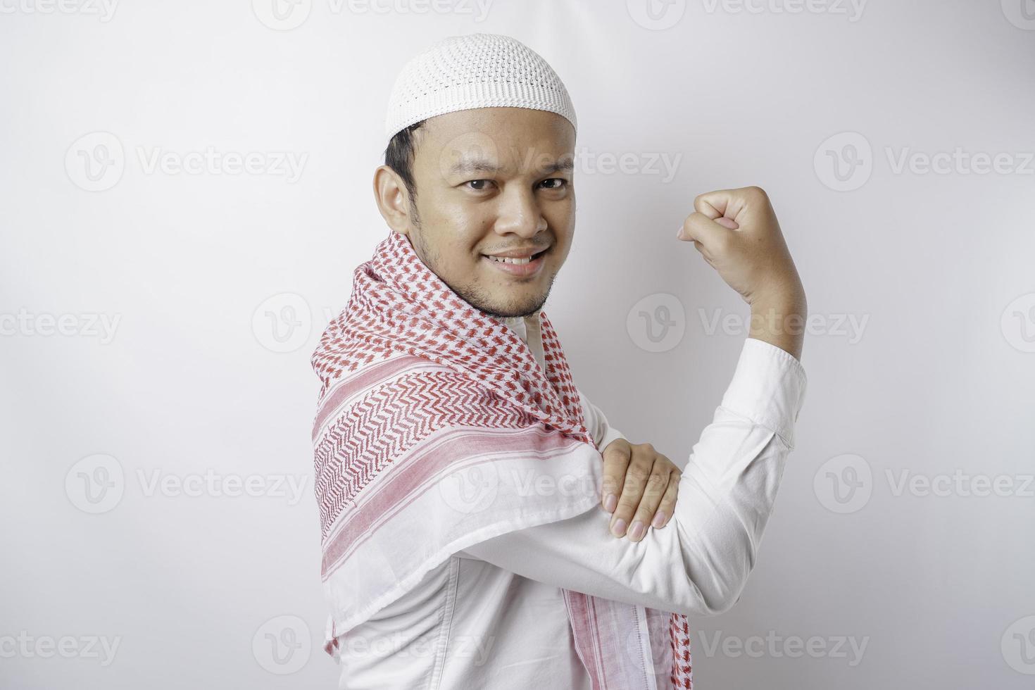 hombre musulmán asiático emocionado que muestra un gesto fuerte levantando los brazos y los músculos sonriendo con orgullo foto