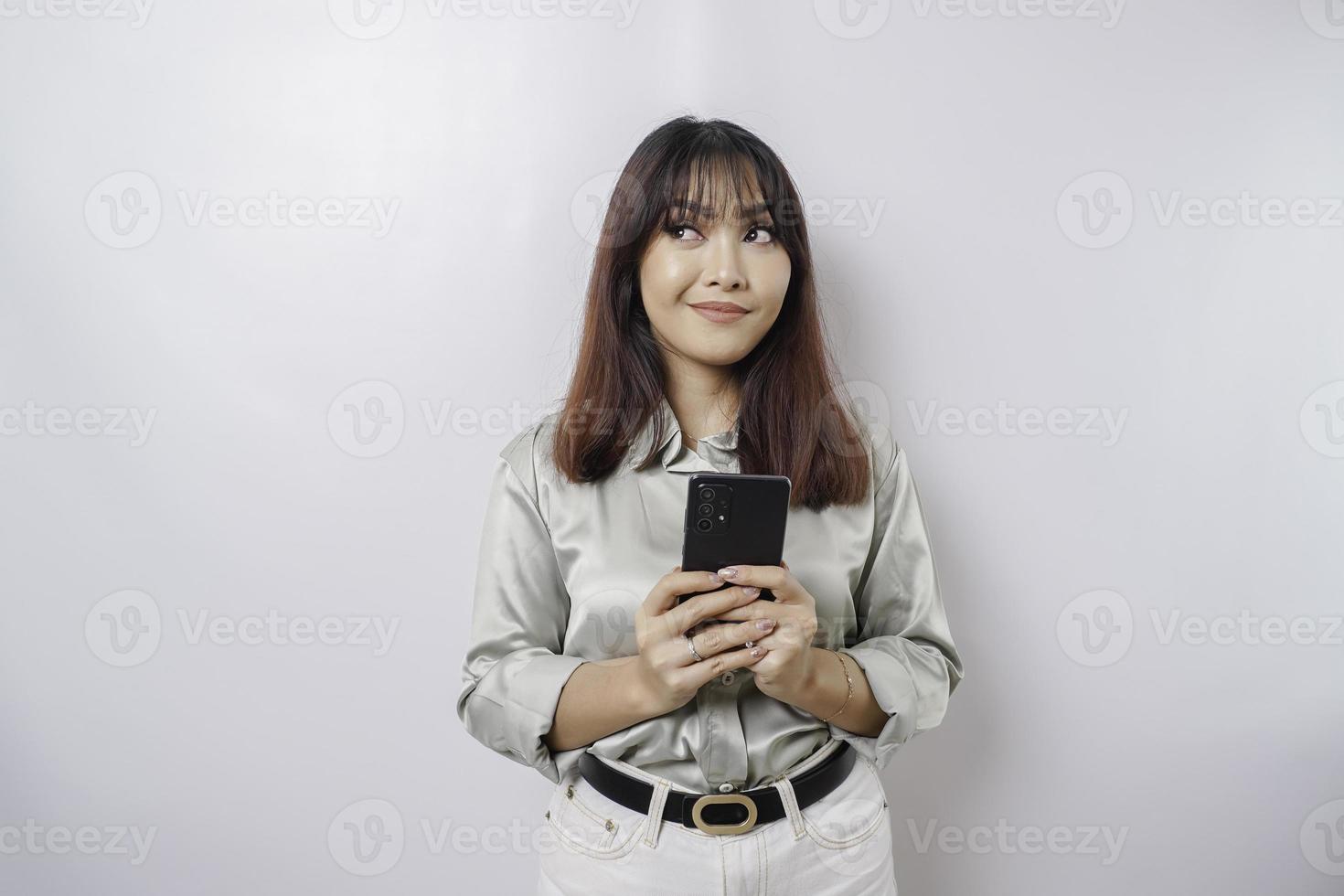 Photo of a thoughtful young woman holding her phone and looking aside. isolated on white color background