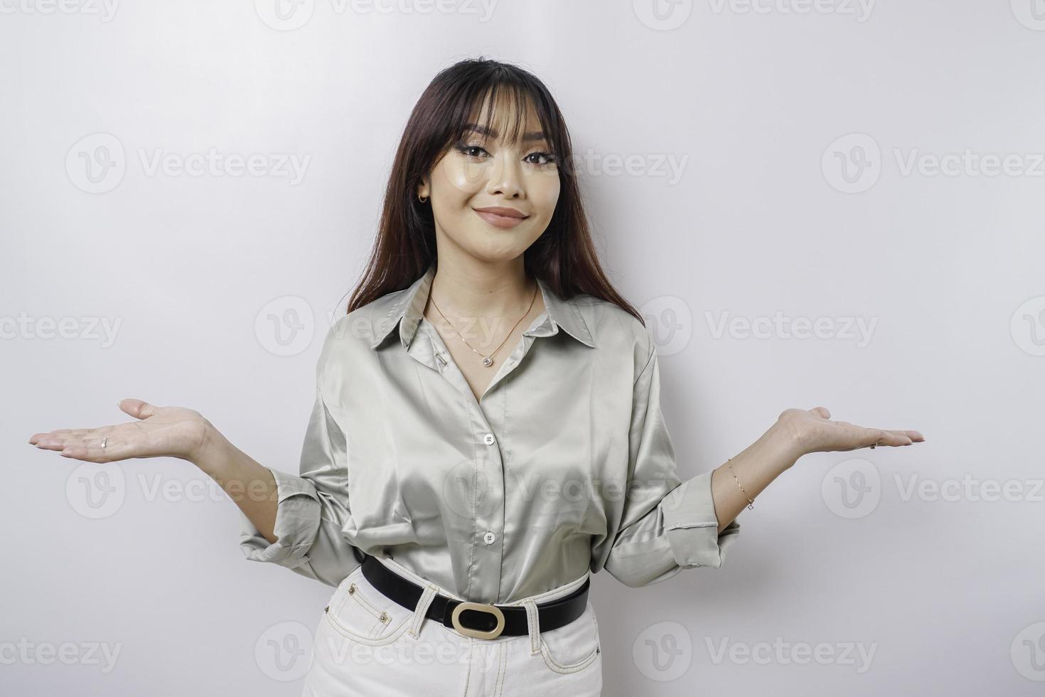 Excited Asian woman wearing sage green shirt pointing at the copy space beside her, isolated by white background photo