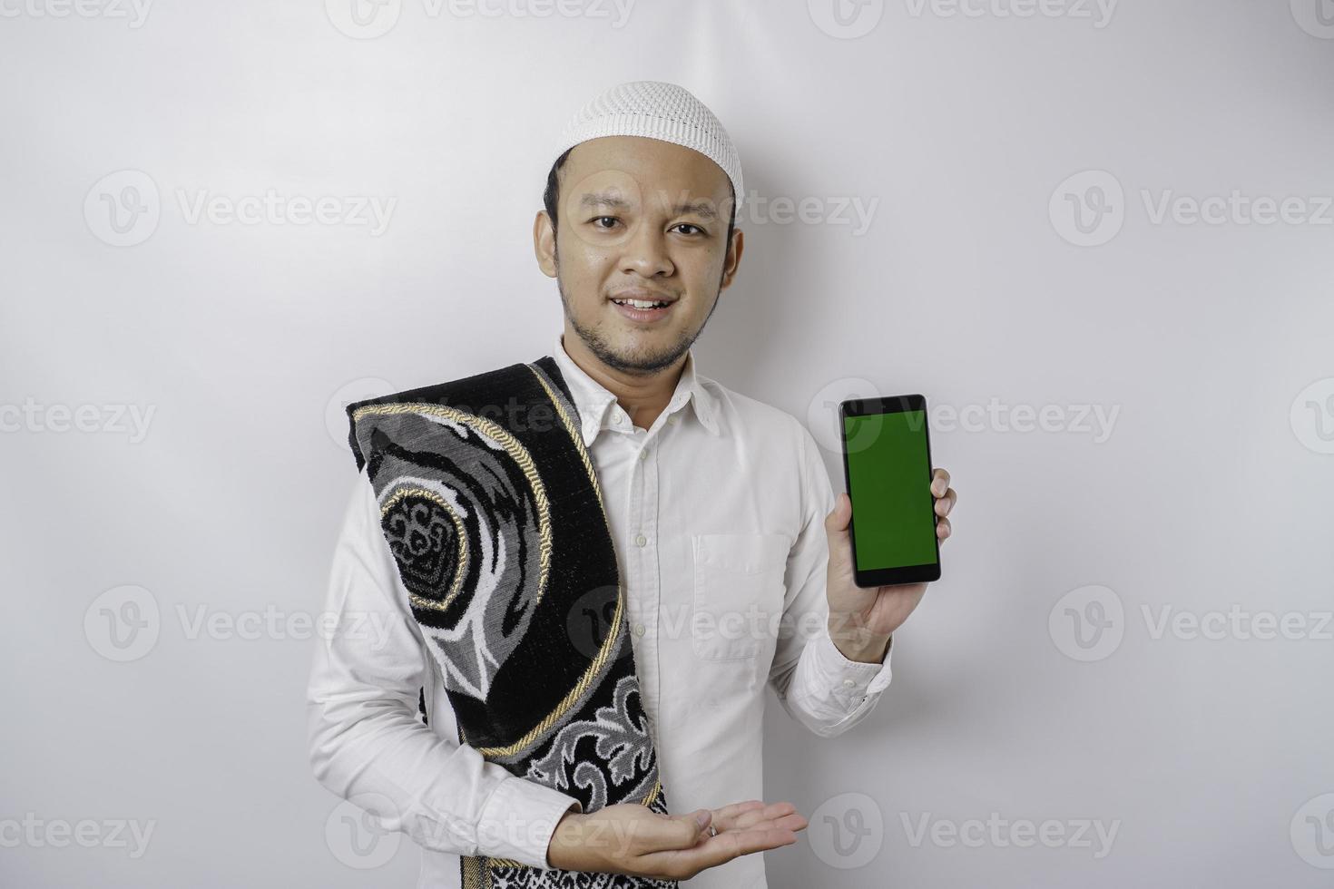 A portrait of a happy Asian Muslim man smiling while showing copy space on his phone, isolated by white background photo
