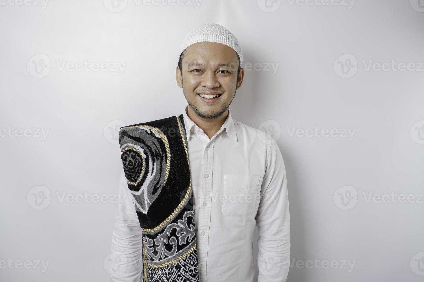A portrait of a happy Asian Muslim man with prayer rug on his shoulder is smiling isolated by white background photo