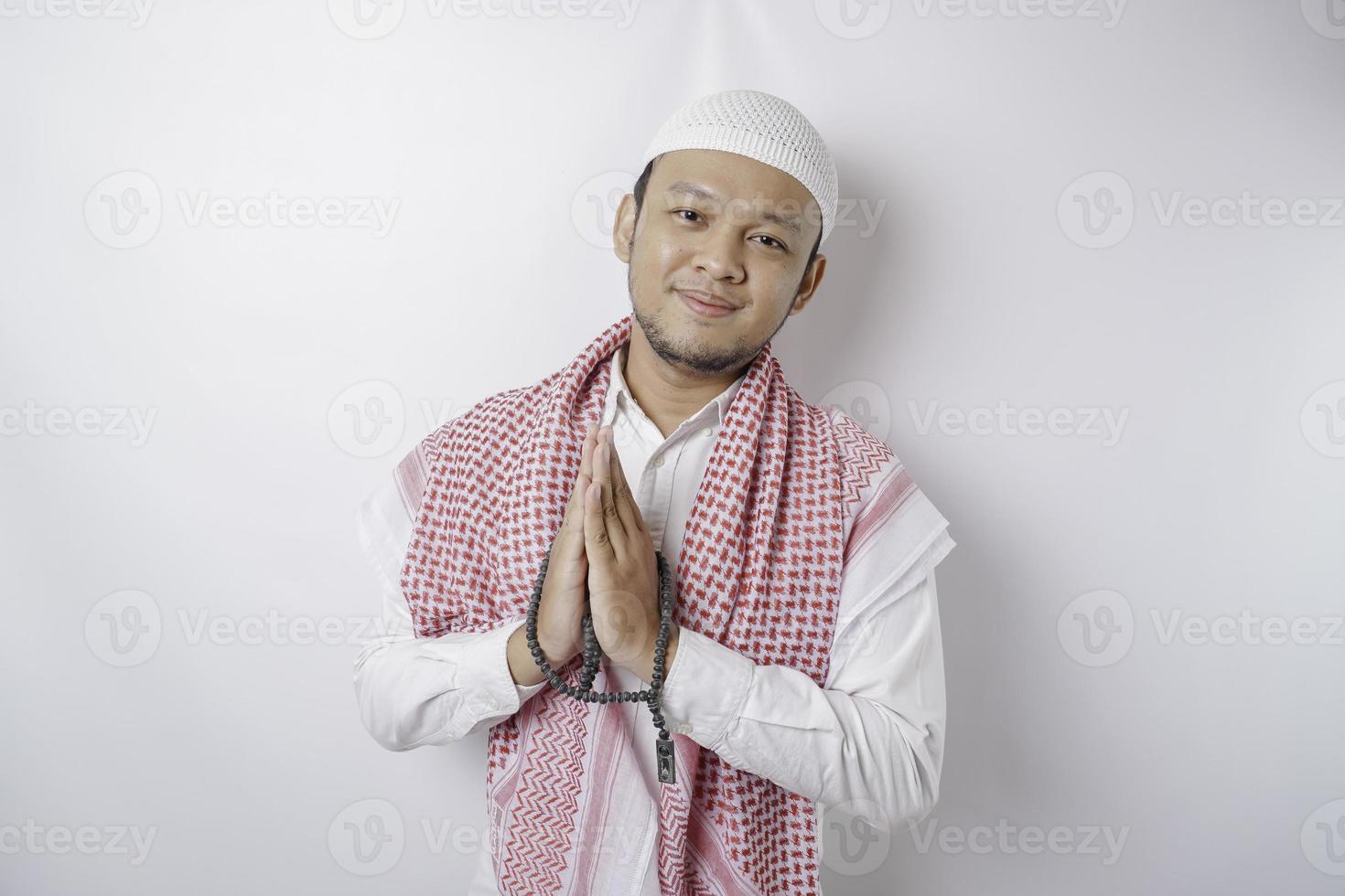 Smiling young Asian Muslim man, gesturing traditional greeting isolated over white background photo