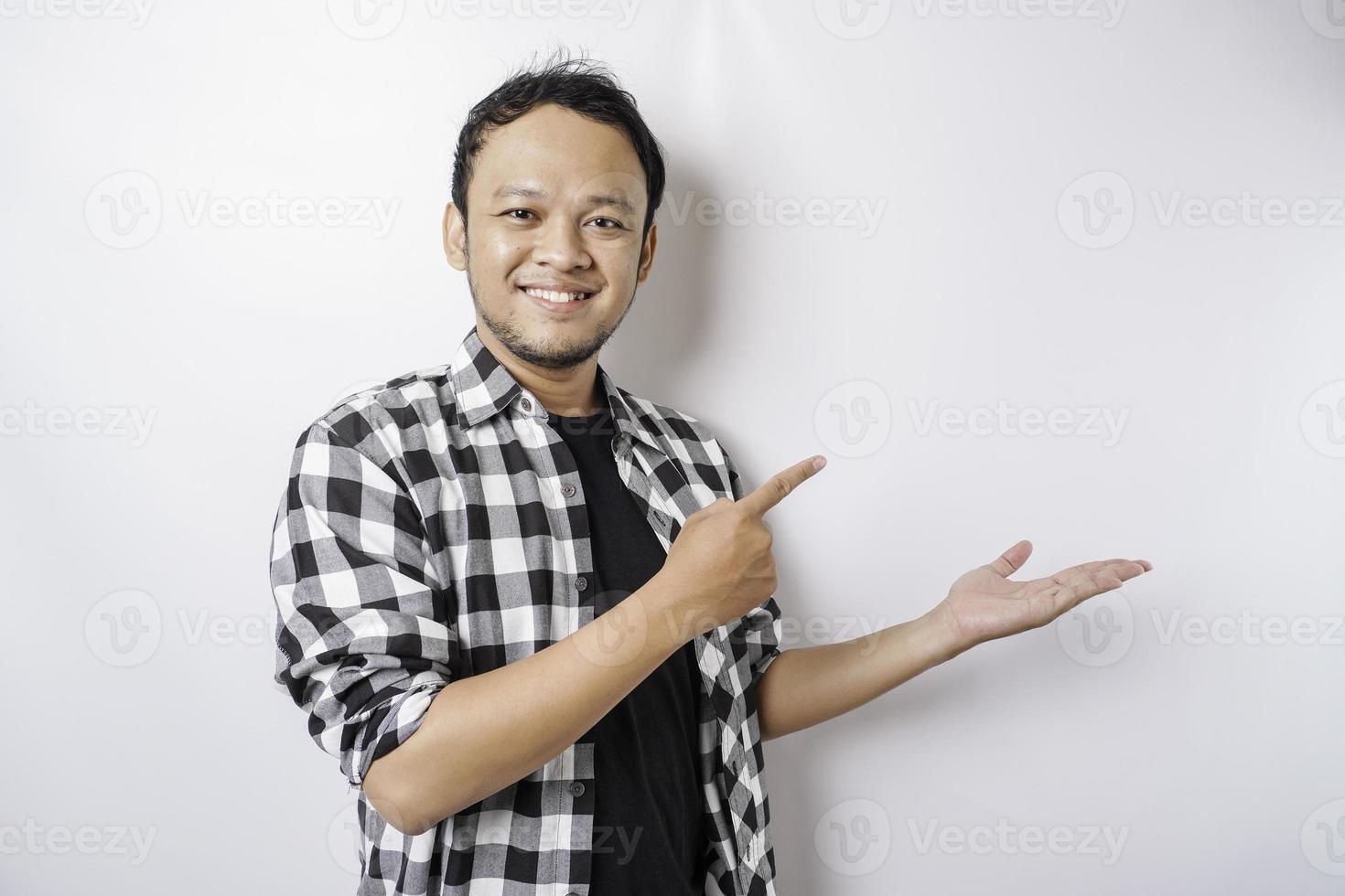 Excited Asian man wearing tartan shirt is pointing at the copy space beside him, isolated by white background photo