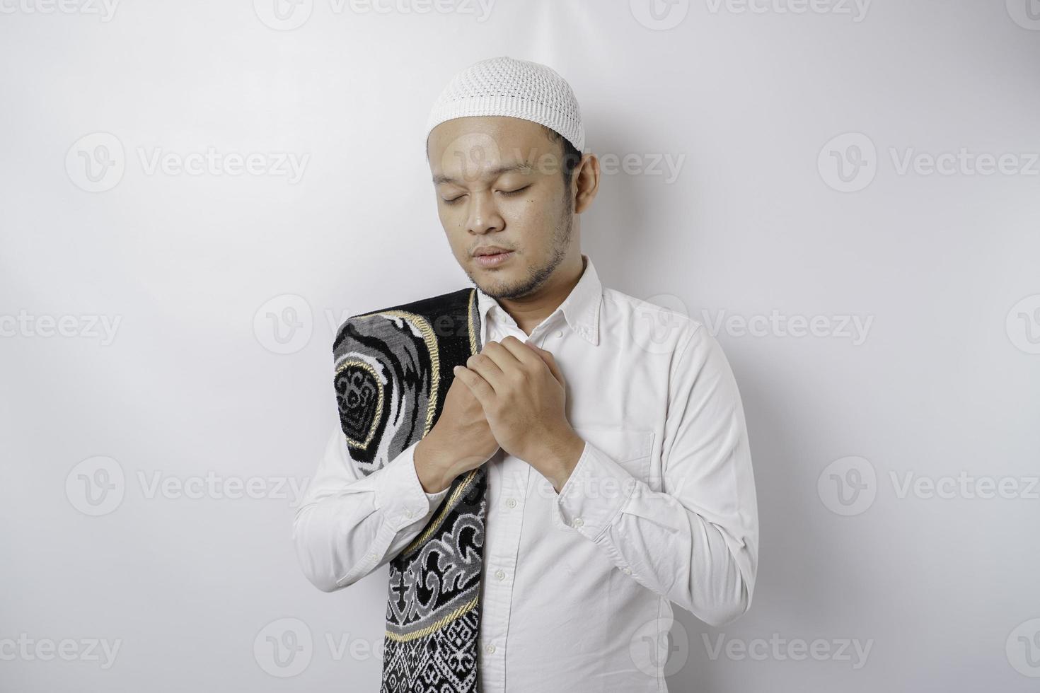 Happy handsome Asian Muslim man with prayer rug on his shoulder is praying to God. photo